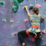 A climber on a rock wall reaches and hangs from a hold, stretching the muscles and nerves through the shoulder and down the arm,