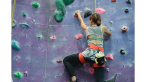 A climber on a rock wall reaches and hangs from a hold, stretching the muscles and nerves through the shoulder and down the arm,
